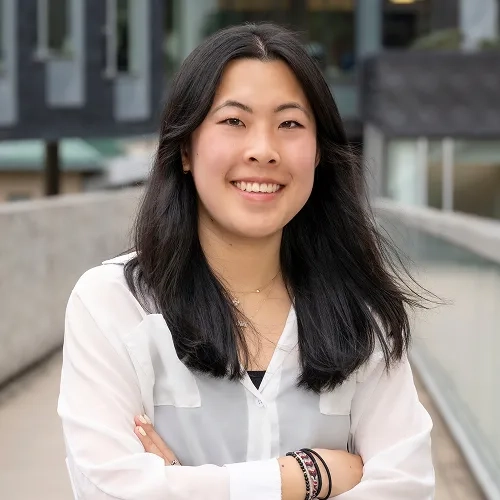 Sarah Chen wears a white button down shirt and smiles with crossed arms near the Gates and Hillman Centers on CMU campus.