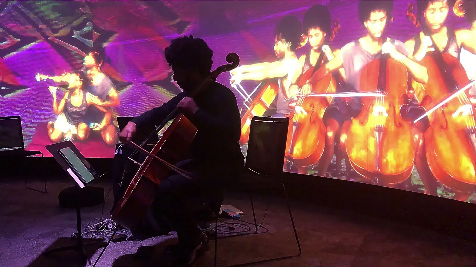 Student playing cello with video playing around them.