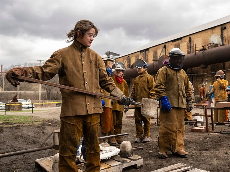 CMU student wearing leather protective gear, pouring iron into molds.