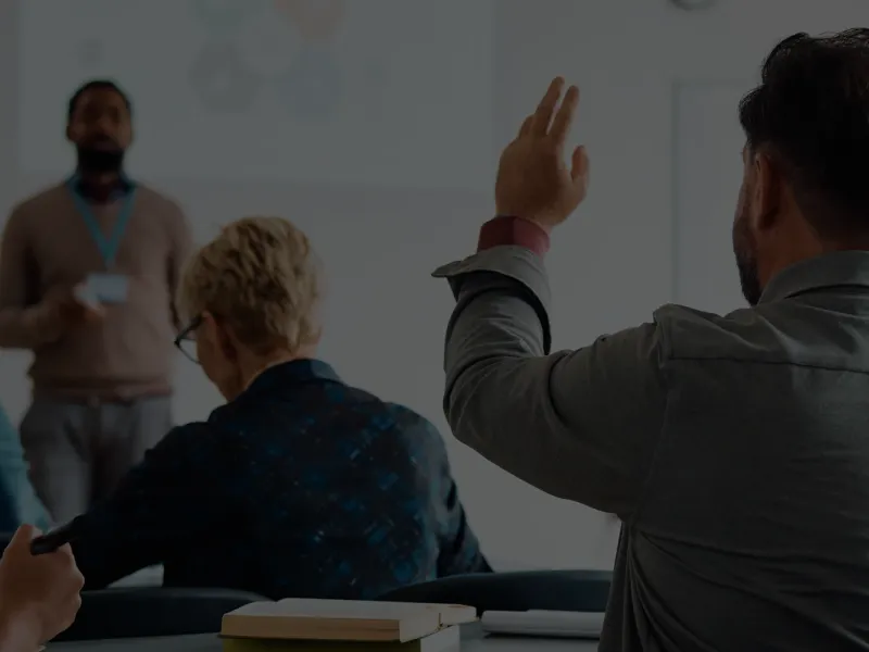 Several people in a classroom with one person raising his hand