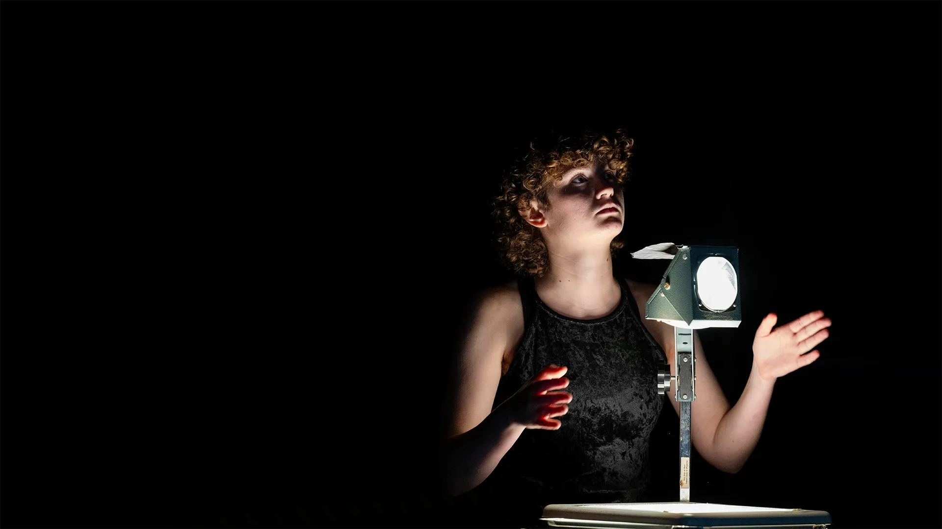 Carnegie Mellon student at an opera rehearsal, their face and hands dramatically lit by an old overhead projector.
