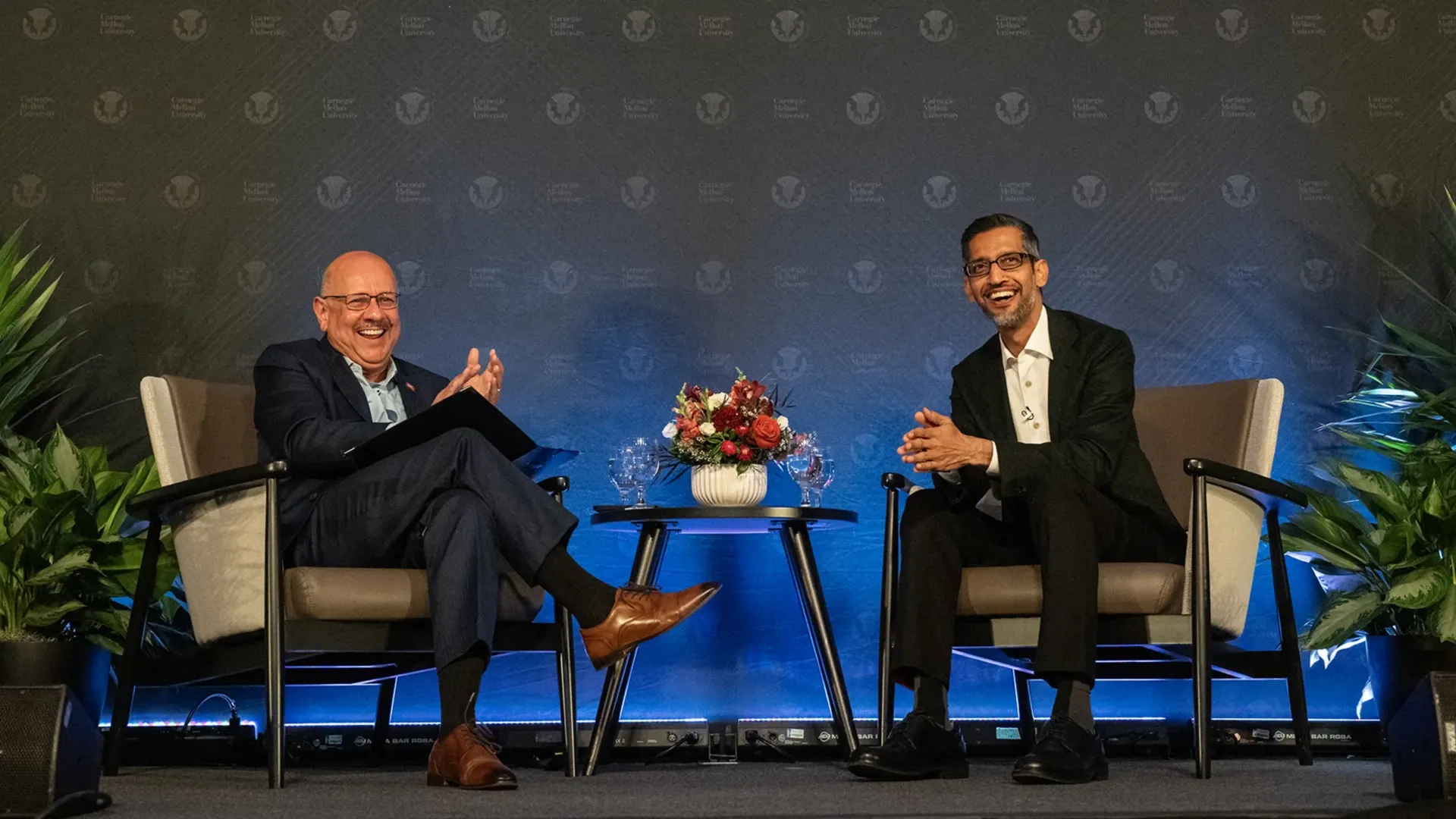 CMU President Jahanian and Sundar Pichai smile and sit in front of a dark blue background.