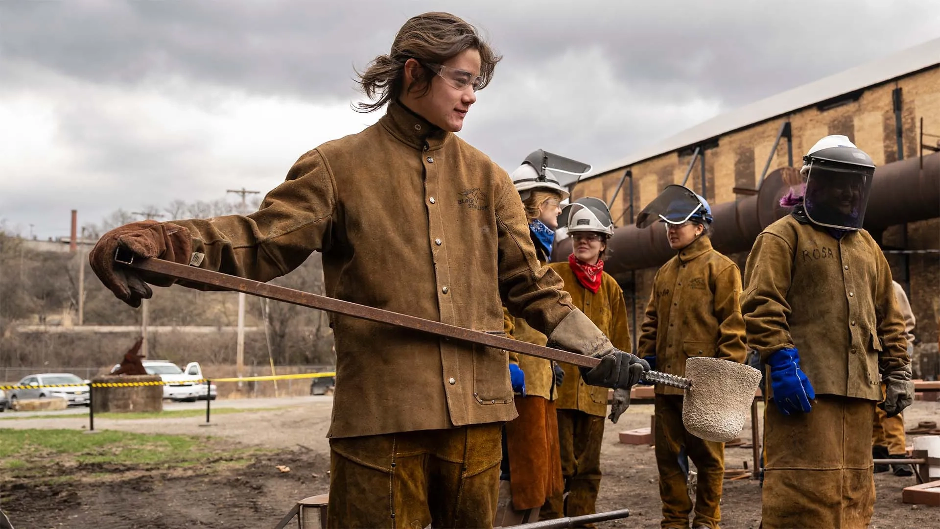 CMU student wearing leather protective gear, pouring iron into molds.