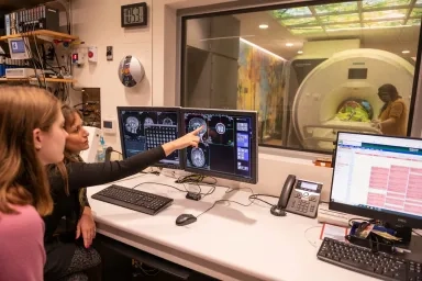 Two people looking at a brain scan on a computer with an MRI machine in the background