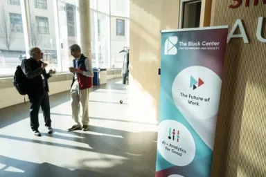 Two people stand in a hallway talking near a banner for the Block Center for Technology and Society