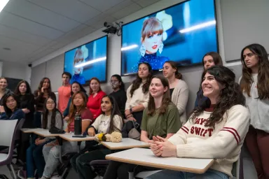 Several students in class with images of Taylor Swift on screens behind them